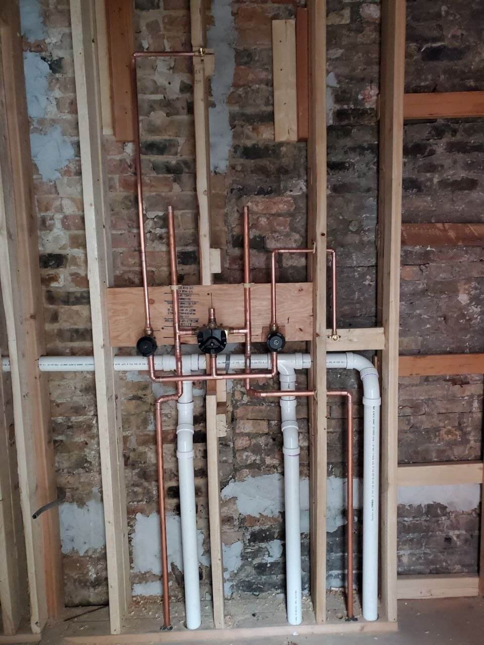 Copper water supply lines and shut-off valves installed inside an exposed brick wall