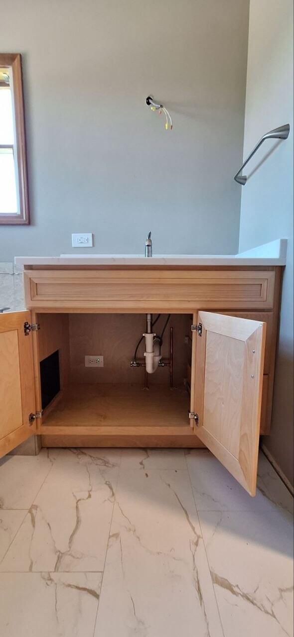Bathroom vanity faucet installed above an open cabinet with plumbing visible